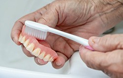 Man brushing his removable dentures over a sink