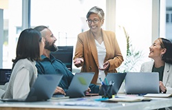 Woman in tan jacket with gray hair presenting to co-workers