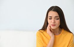 Woman in yellow shirt rubbing cheek due to tooth pain.